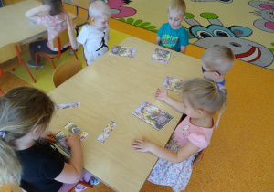 Pięcioro dzieci siedzi przy stole i składa z części obrazek łąki.